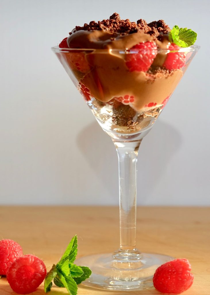 Chocolate pudding layered with chocolate sand and fresh raspberries served in a martini glass garnished with Chocolate Sand and fresh mint.
