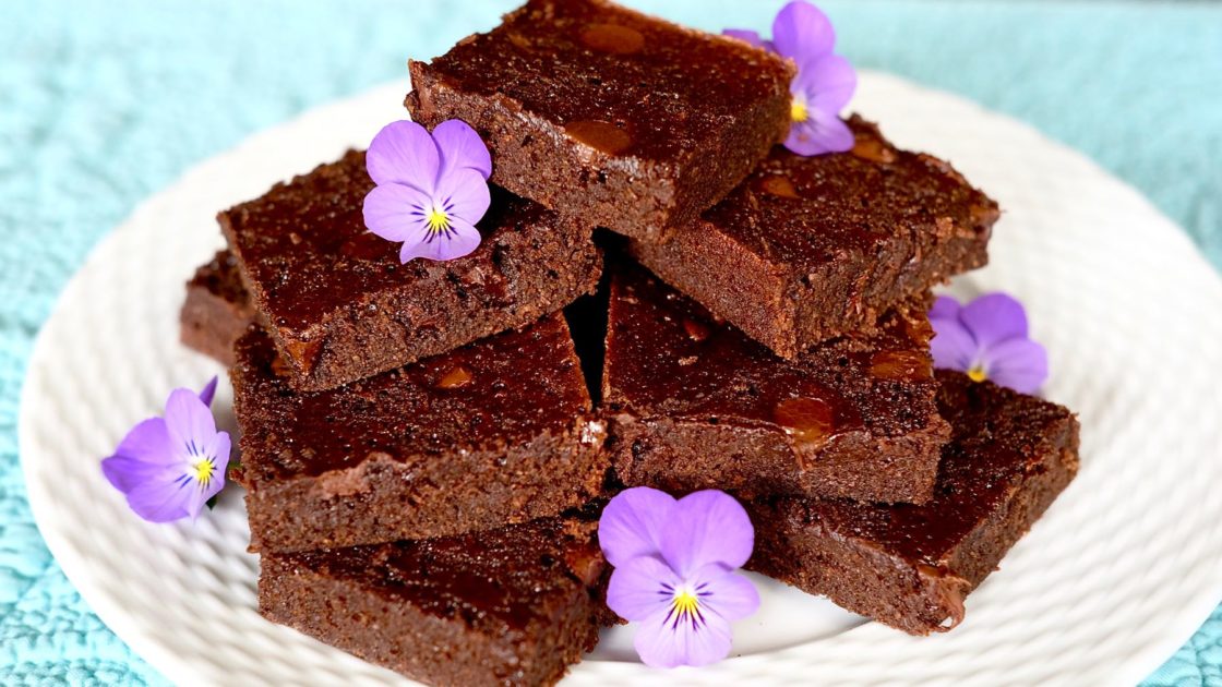 Double chocolate Brownies on white plate garnished with lavender violas
