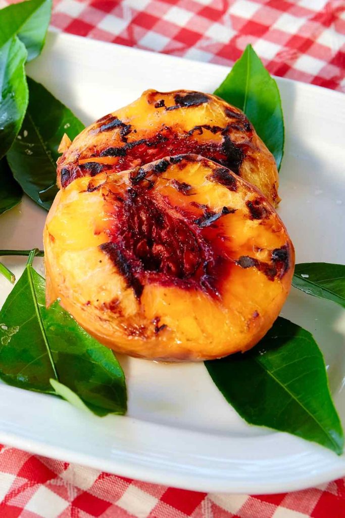 Grilled Peach halves on white plate with red and white checkered underlay.