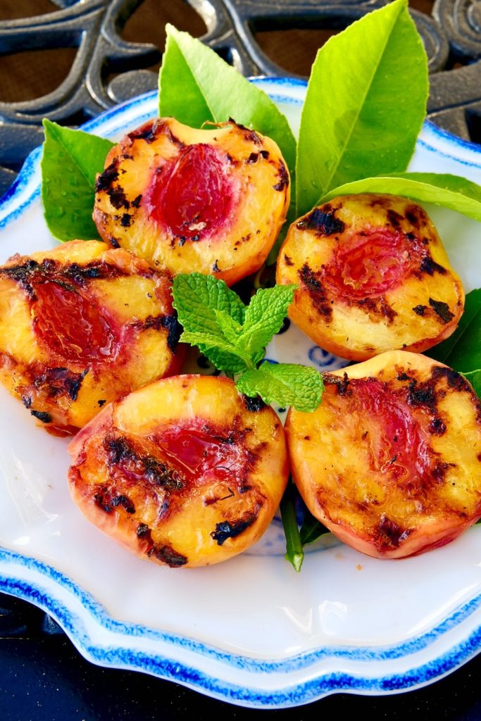 Grilled Peach halves displayed on a white and blue plate with lemon and mint leaves.