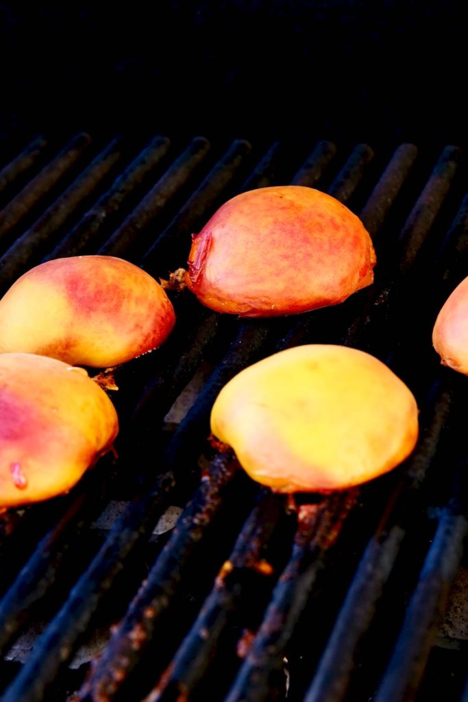 Peach halves being grilled on a gas barbecue.
