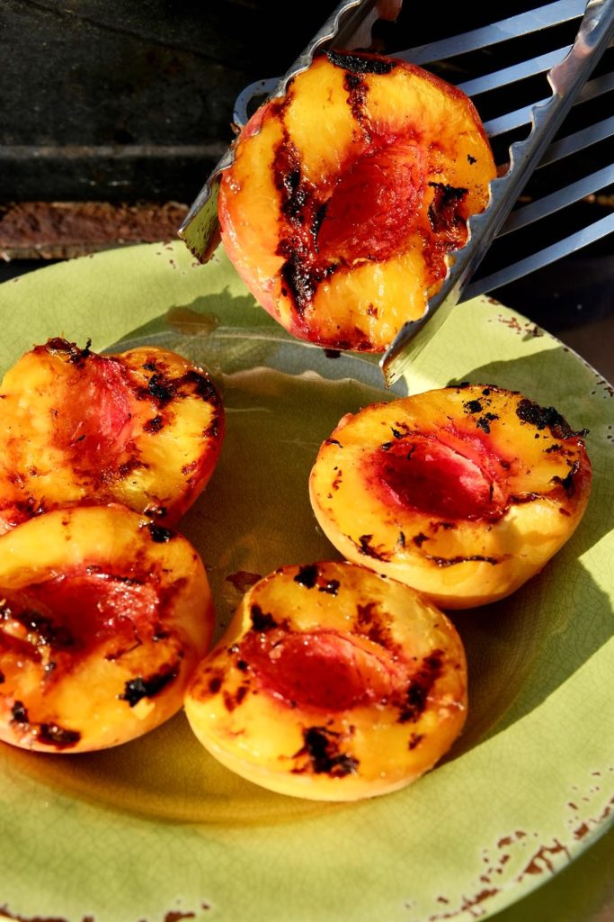 Grilled Peach halves being removed from grill and plated on green plate.