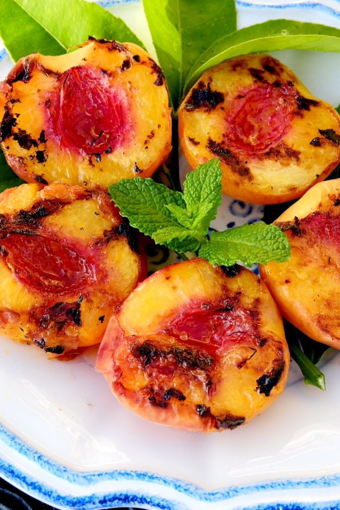 Grilled Peach halves on white and blue plate garnished with mint and lemon leaves.