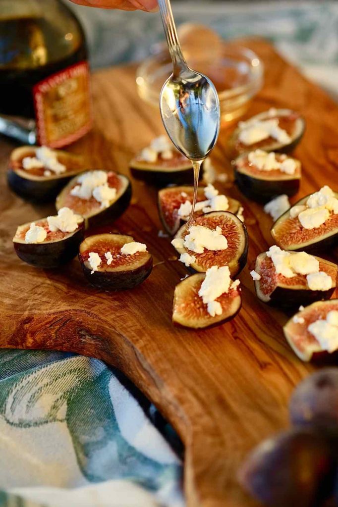 Easy Fig Appetizer with Goat Cheese and drizzled with honey served on an olive wood board