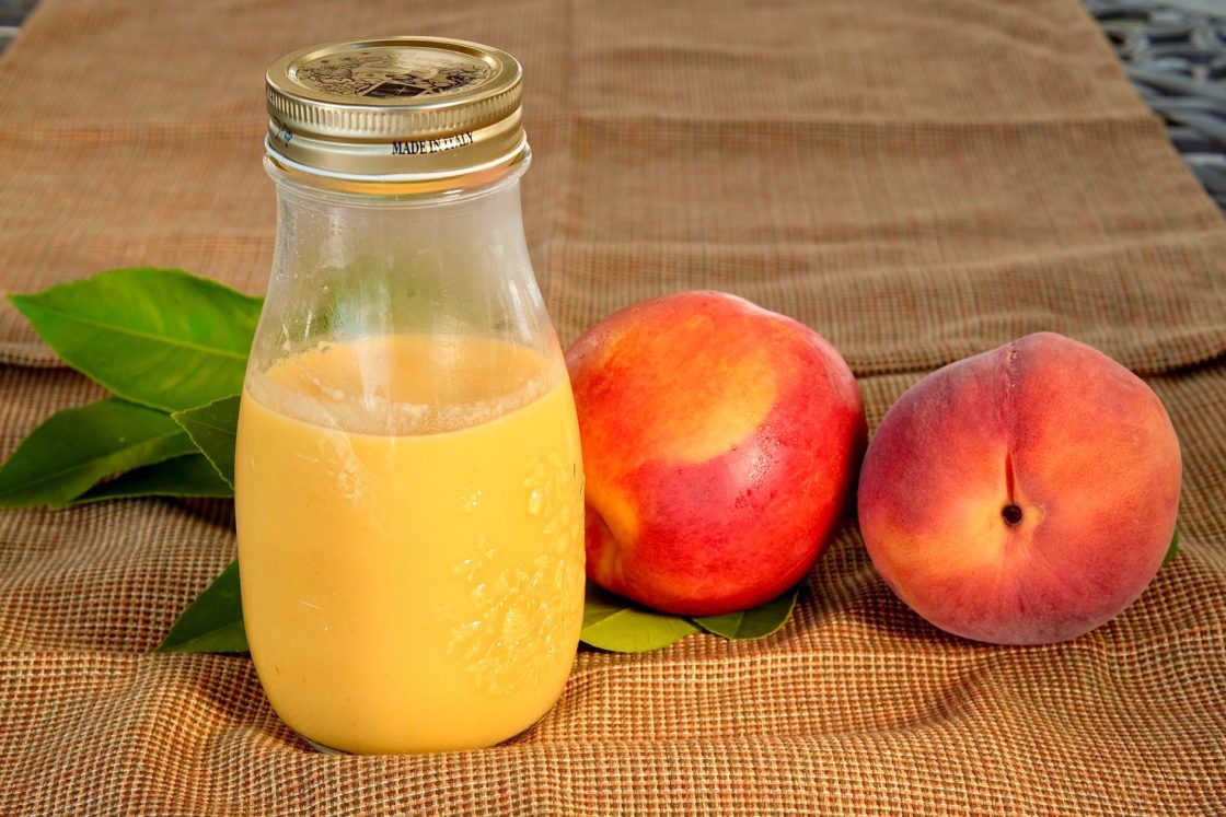 Fresh Peach Vinaigrette in glass jar next to a fresh peach and nectarine