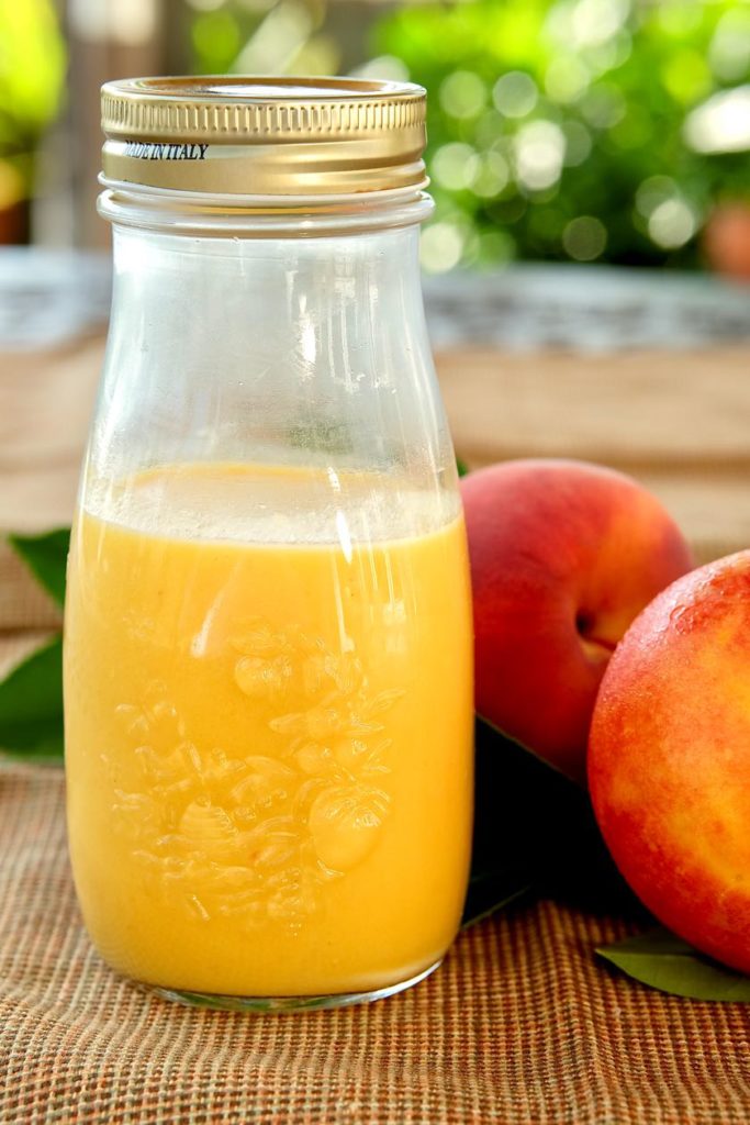 Fresh Peach Vinaigrette in glass jar with fresh peach and nectarine in background.