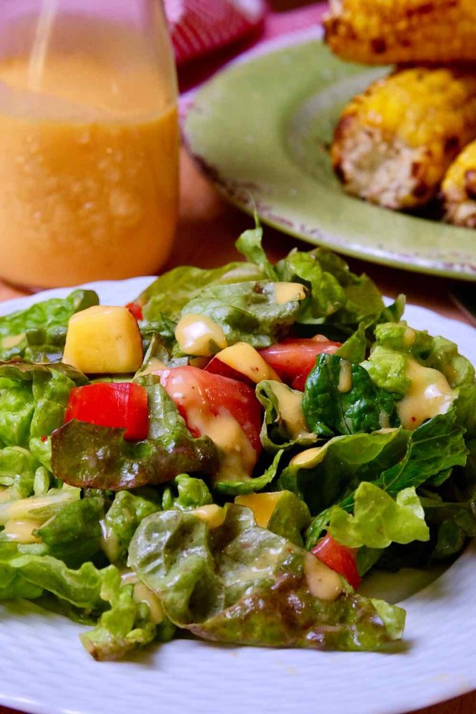 Green salad dressed with Fresh Peach Vinaigrette on white plate with bottle of dressing in background.