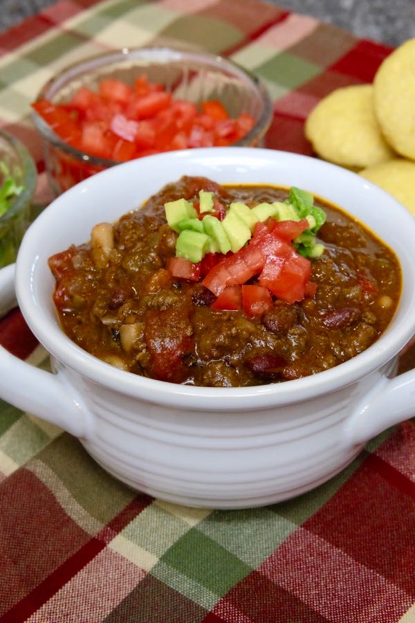 Hearty Bison Chocolate Chili in white bowl with chopped tomato and avocado in background.