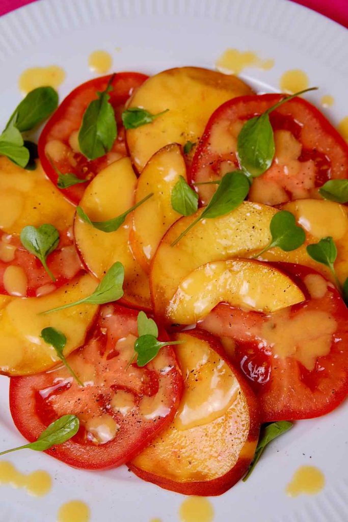 Peach and Tomato Salad arranged on white plate and drizzled with Peach Vinaigrette and garnished with baby arugula sprouts.
