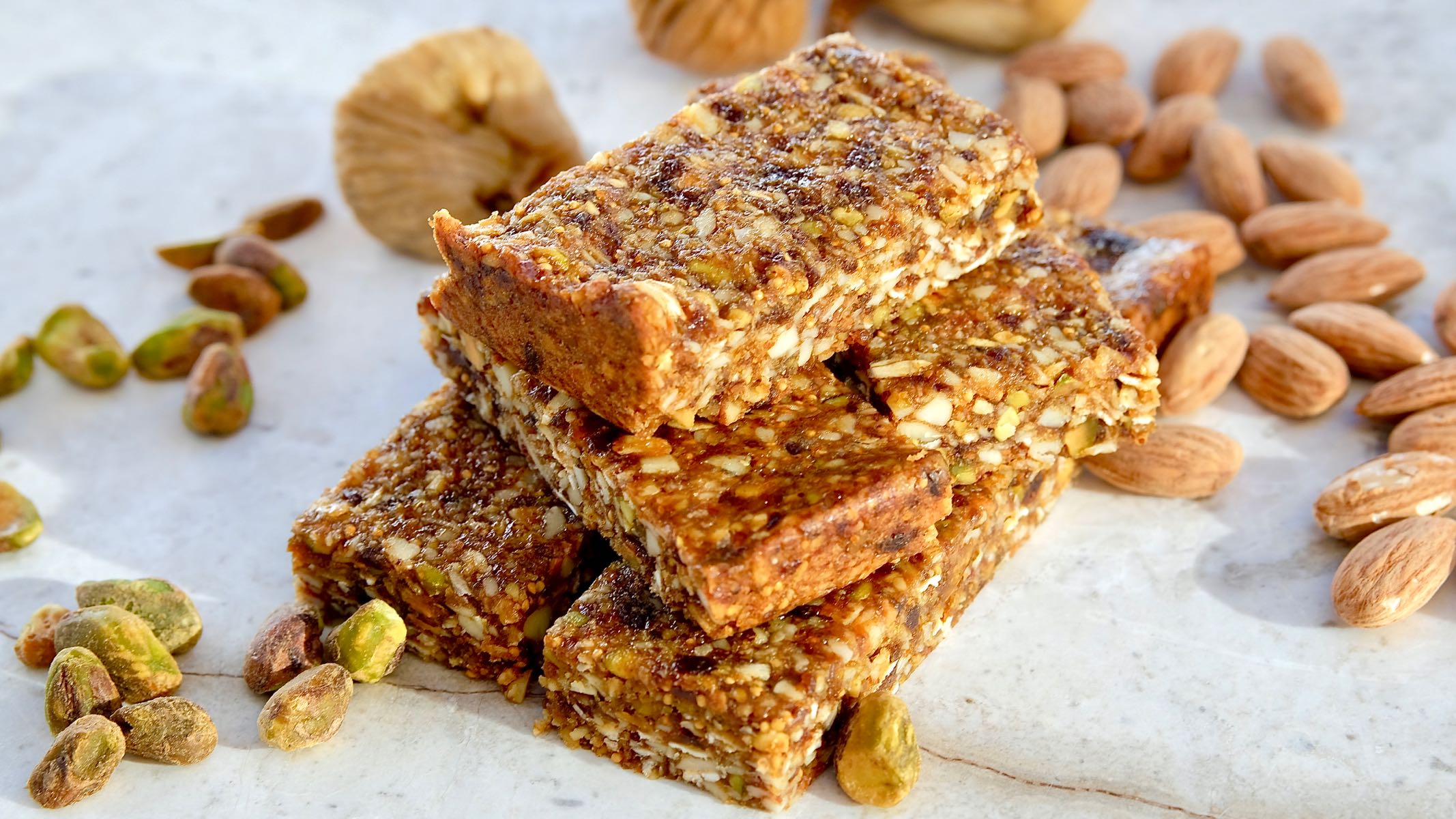 Chewy Almond Fig Granola Bars on white marble with almonds, dried figs and pistachios in background