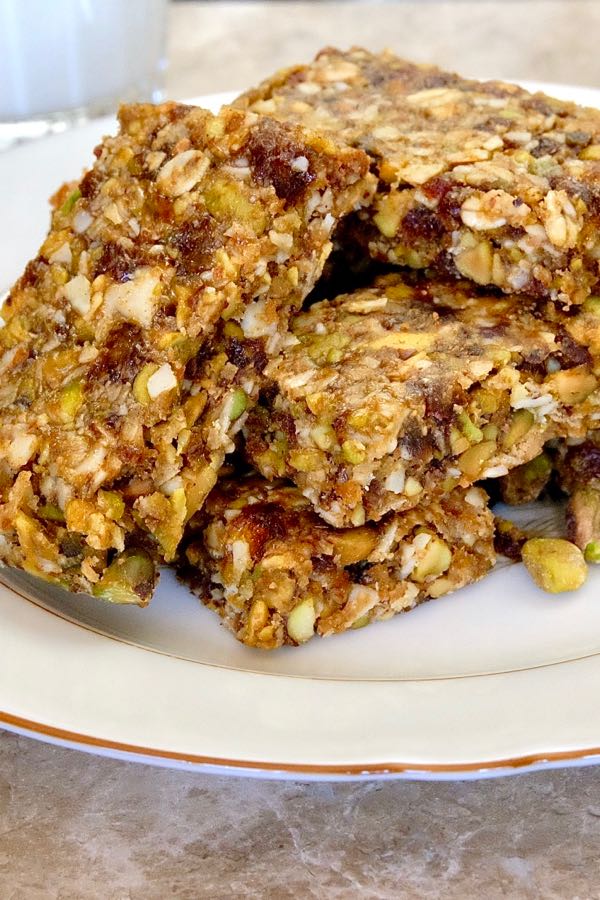 Pistachio Apricot Granola Bars stacked on beige plate with glass of milk in background.