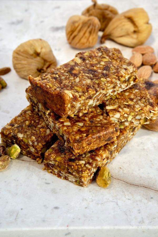 Chewy Almond Fig Granola Bars stacked on white marble with pistachios, almonds and dried figs scattered in background