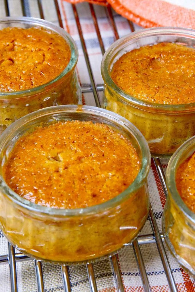 Pumpkin Custard baked in individual glass cups set on cooling rack with orange trimmed linen in background