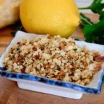 Toasted Breadcrumb Gremolata in square dish on olive wood board with bread, lemon and parsley in background