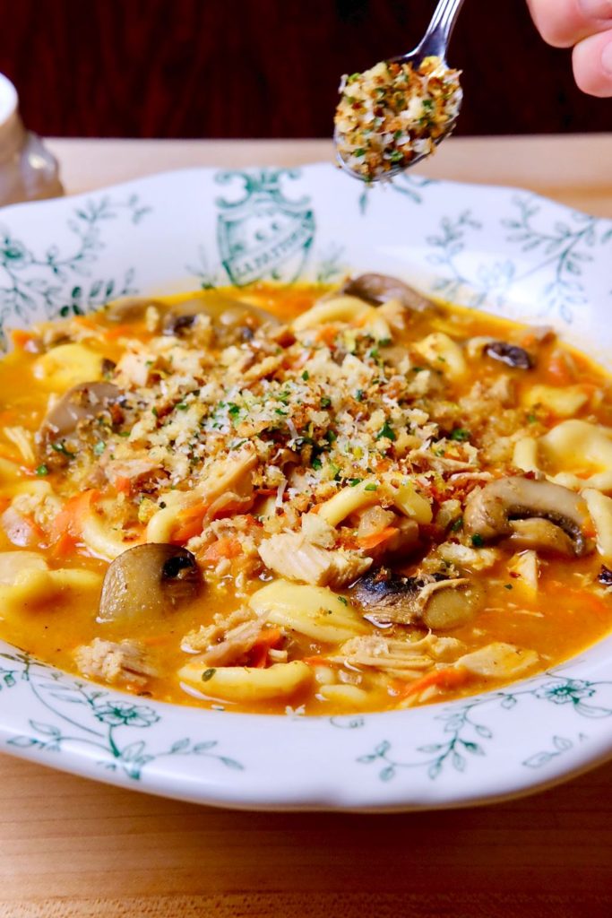 White and green soup bowl of Turkey Tetrazzini Soup being garnished with Breadcrumb Gremolata