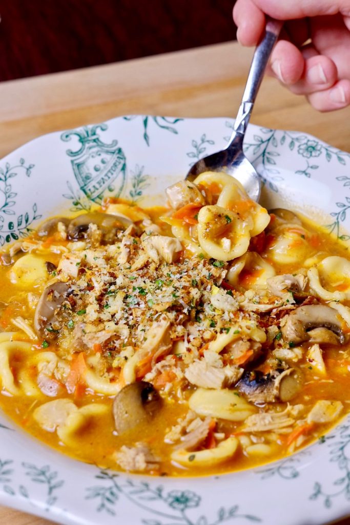 Green and white soup bowl with a bite shot of Turkey Tetrazzini and toasted breadcrumb gremolata in small bowl in background>