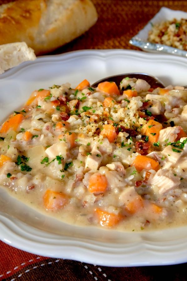 Turkey Chowder served in white soup bowl garnished with breadcrumb gremolata.  Loaf of French bread is set in background.
