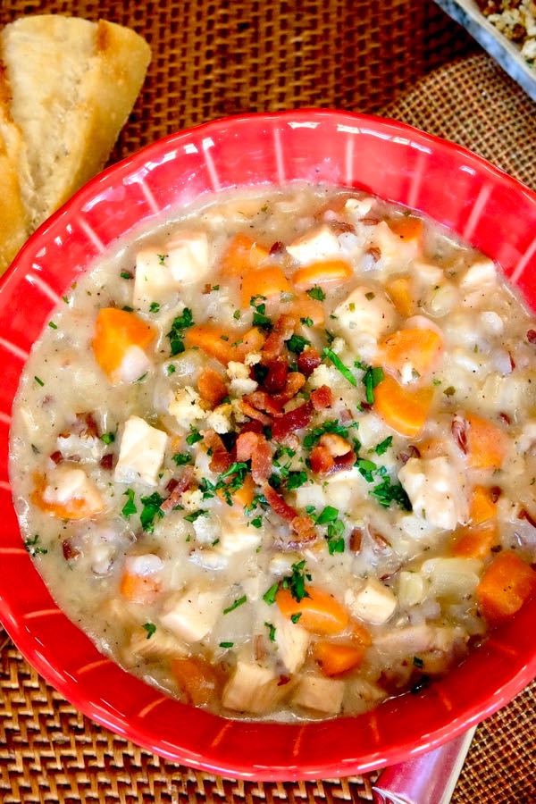 Hearty Turkey Chowder in red soup bowl with french baguette in background