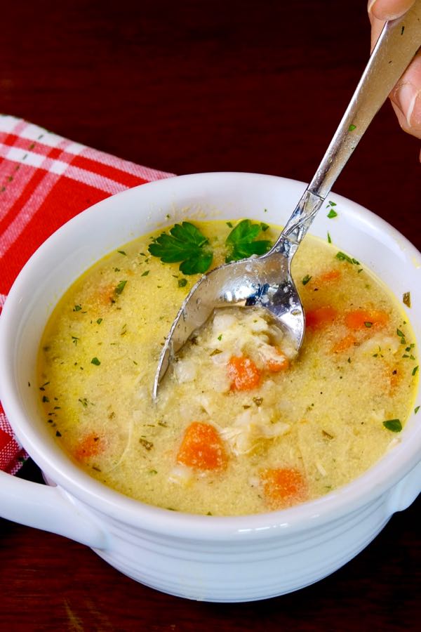 Greek-Style Lemon Chicken Soup in White soup bowl with red linen napkin in background
