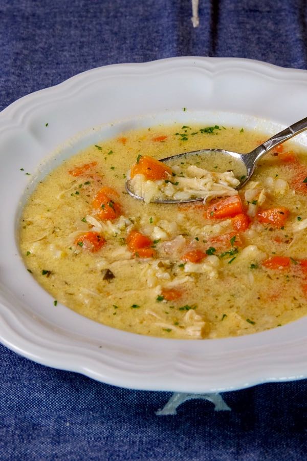 Greek-Style Lemon Chicken Soup in white bowl with blue linen underlay.