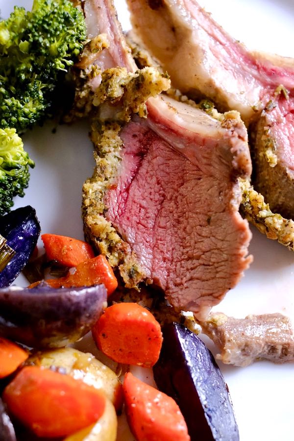Herb-Crusted Rack of Lamb served on white plate with broccoli and Colorful Roasted Potatoes. 