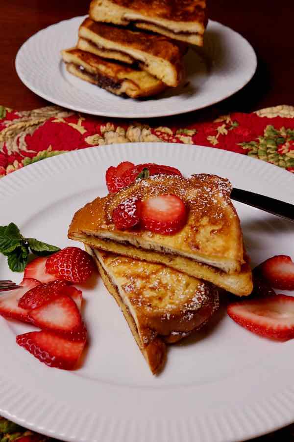 Nutella and Mascarpone Stuffed French Toast served cut in wedges on white plate with sliced strawberries.