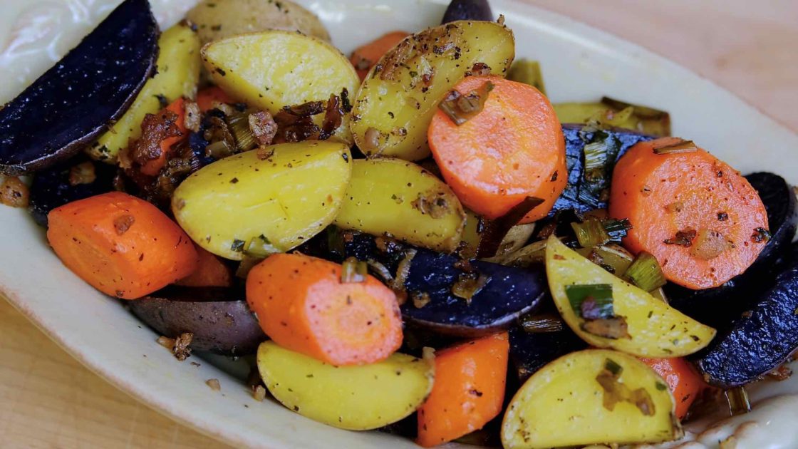 Colorful Roasted Baby Potatoes with carrots in beige serving bowl set on maple board