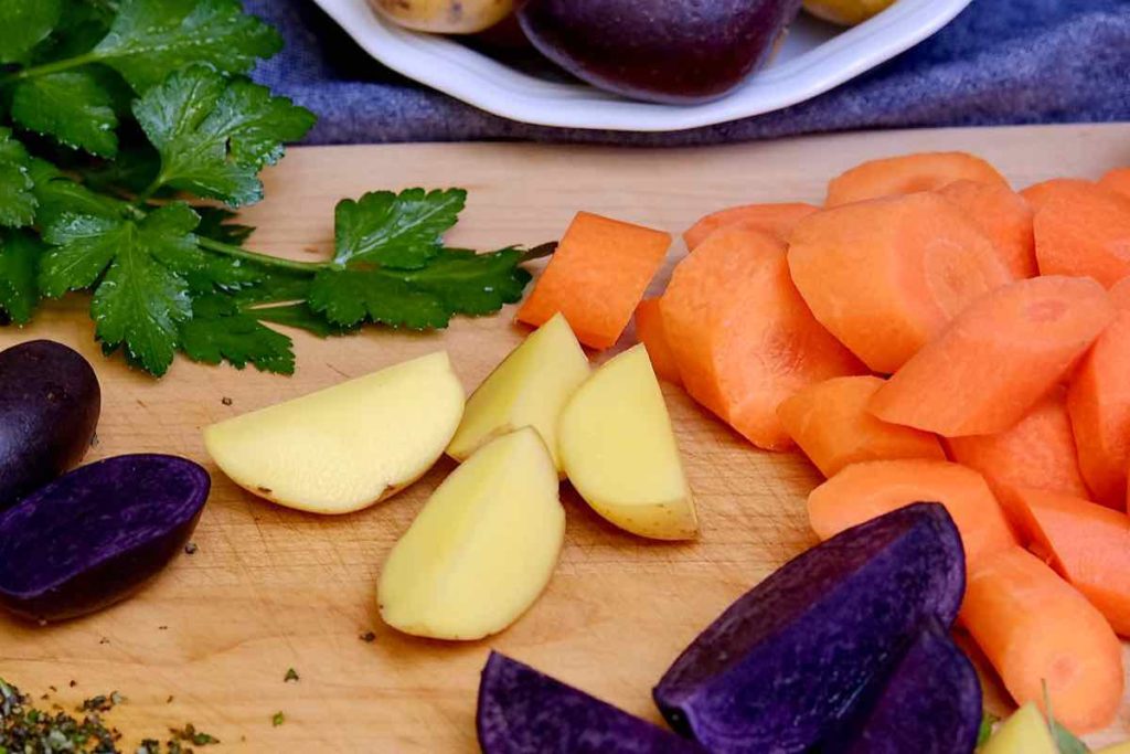Purple and Gold Potatoes, Carrots and herbs on cutting board being prepped for Colorful Roasted Potatoes