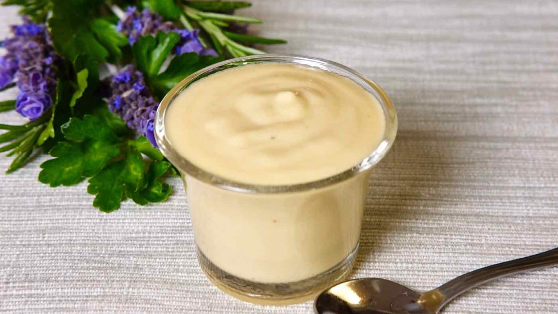 Creamy Dijon Sauce in Glass serving bowl with spoon in fore front and lavender bouquet in background.