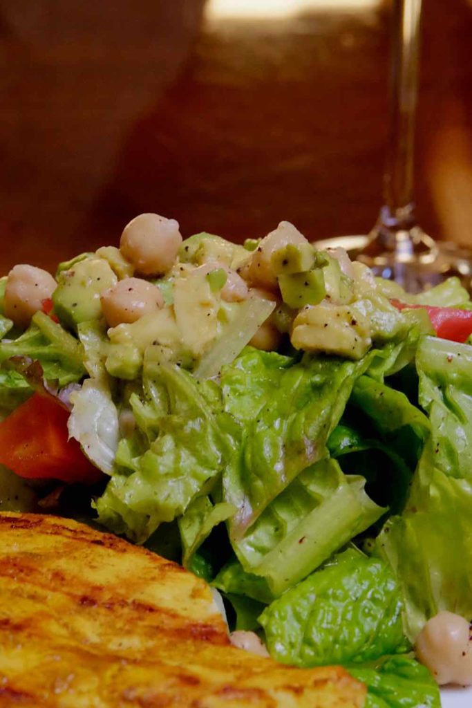 Green Mediterranean Salad on plate with grilled chicken in forefront.