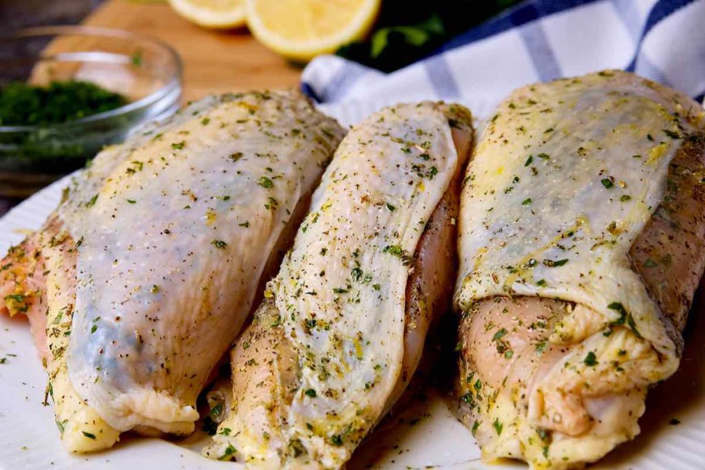 Lemon-Herb Roasted Chicken with herb rub before roasting.  Lemon and parsley in background on a navy and white linen.