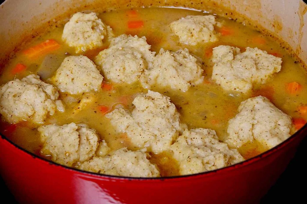 Red braising pot just pulled from the oven with dumplings steamed and cooked in the gravy's surface. 