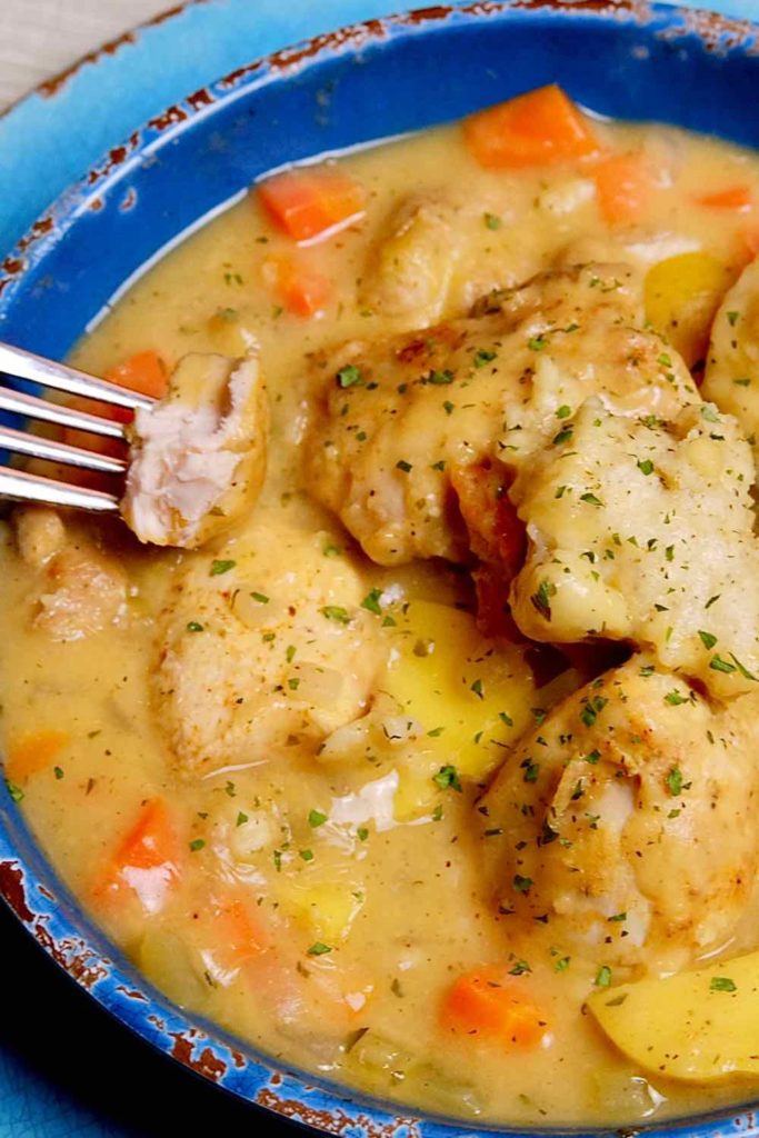 Light Chicken and Dumplings served in a dark blue bowl sitting on a light blue charger plate, with a fork to the left showing a piece of chicken.