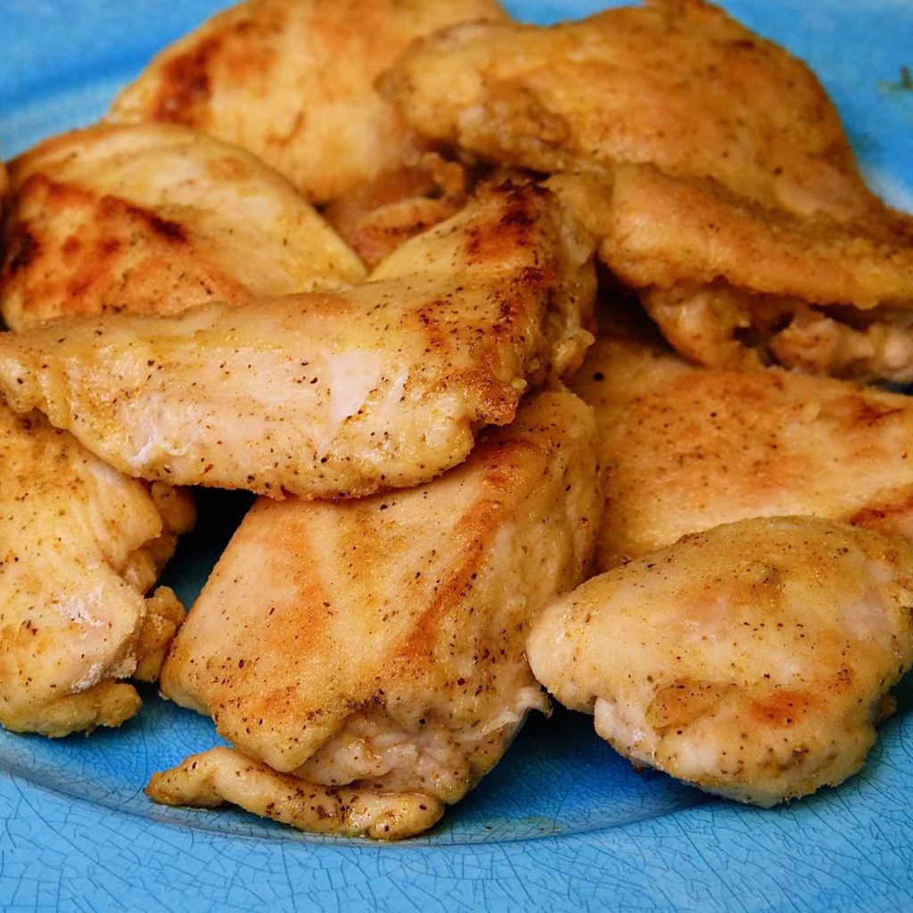 Chicken pieces browned and waiting on a blue plate.