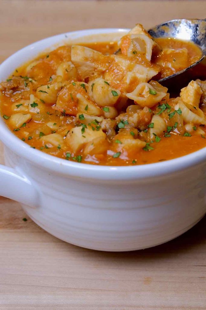 Tuscan Bean Soup in white soup bowl with spoonful of soup.  Backdrop is a maple wood board