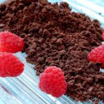 Chocolate Sand garnished with fresh raspberries on ice glass dish set on blue underlay.