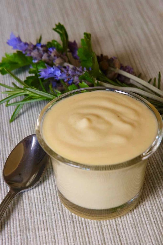 Creamy Dijon Sauce in a glass bowl with beige linen underlay.  Serving to spoon to the left of bowl and lavender bouquet flowers in background.