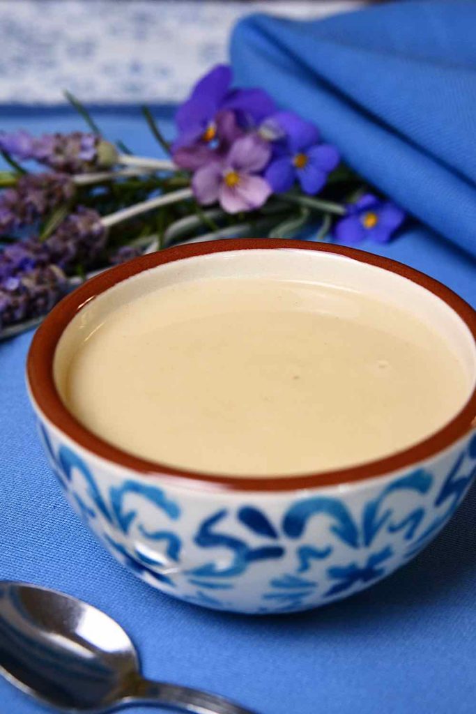 Light Creamy Parmesan Sauce in a white and blue bowl set on a blue and white linen underlay, with a bouquet of lavender and violas in background.