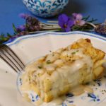 Light Creamy Parmesan Sauce drizzled over Ham and Gruyere Baked French Toast on a withe and blue plate with lavender bouquet and a blue and white bowl with additional sauce in background.