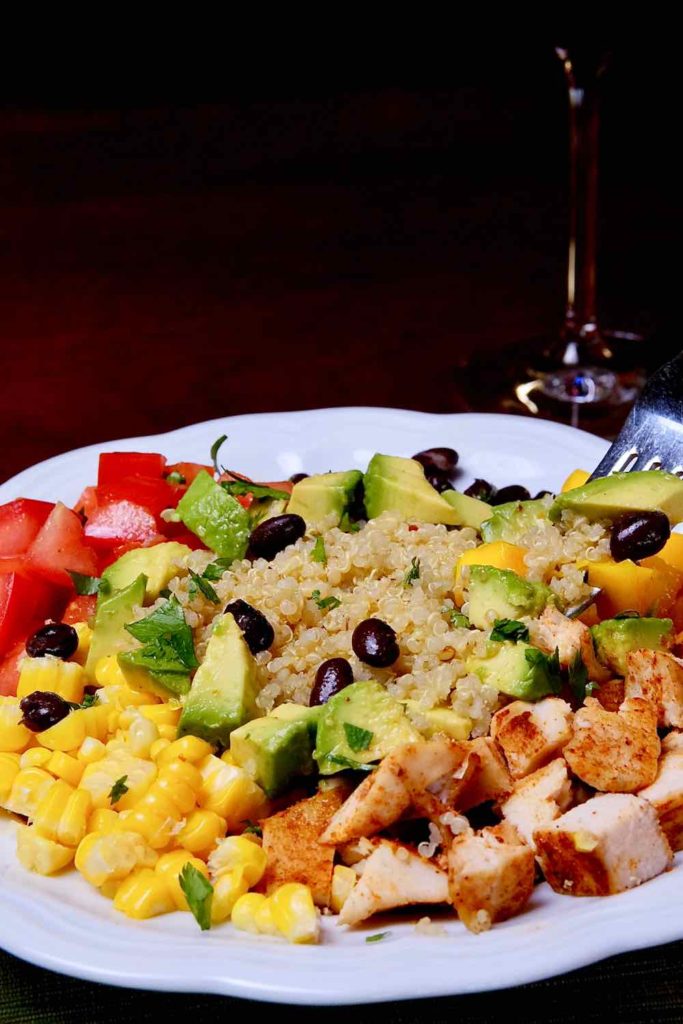 California Chicken Quinoa Bowl served in a white bowl with fork shot of quinoa, avocado, mango and bean.  