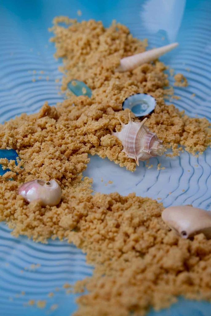 Easy Edible Sand scattered across a blue wavy dish and garnished with baby sea shells.
