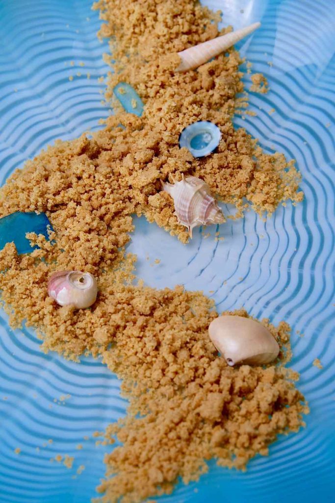Edible Sand scattered on a blue wave dish and garnished with seashells and sea glass.
