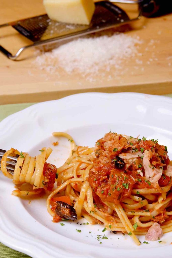 Easy Pasta Puttanesca with Tuna served in white pasta bowl with pasta  twirled on fork.  Pasta is garnished with fresh parsley.