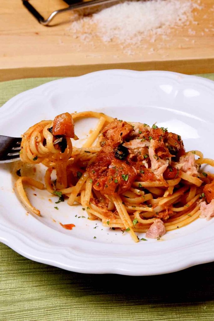 Easy Pasta Puttanesca with Tuna served in white pasta bowl with pasta twirled on fork. 