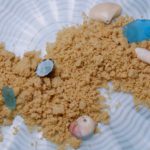 Easy Edible Sand scattered on a blue wavy dish and garnished with sea glass and sea shells.