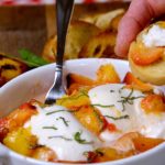 Grilled Peach and Burrata Appetizer served in a white oval terrine dish set on a wood board with red and white checked linen in background.