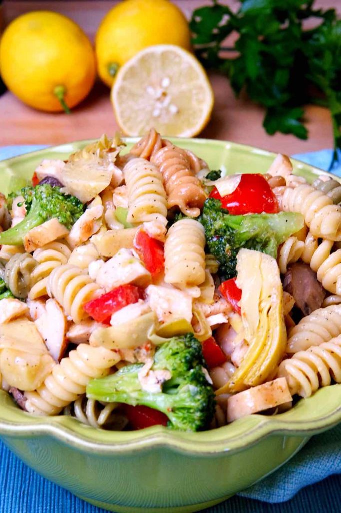 Pasta Salad Italian Style in a green serving bowl with lemon and parsley in background setting on a maple board.
