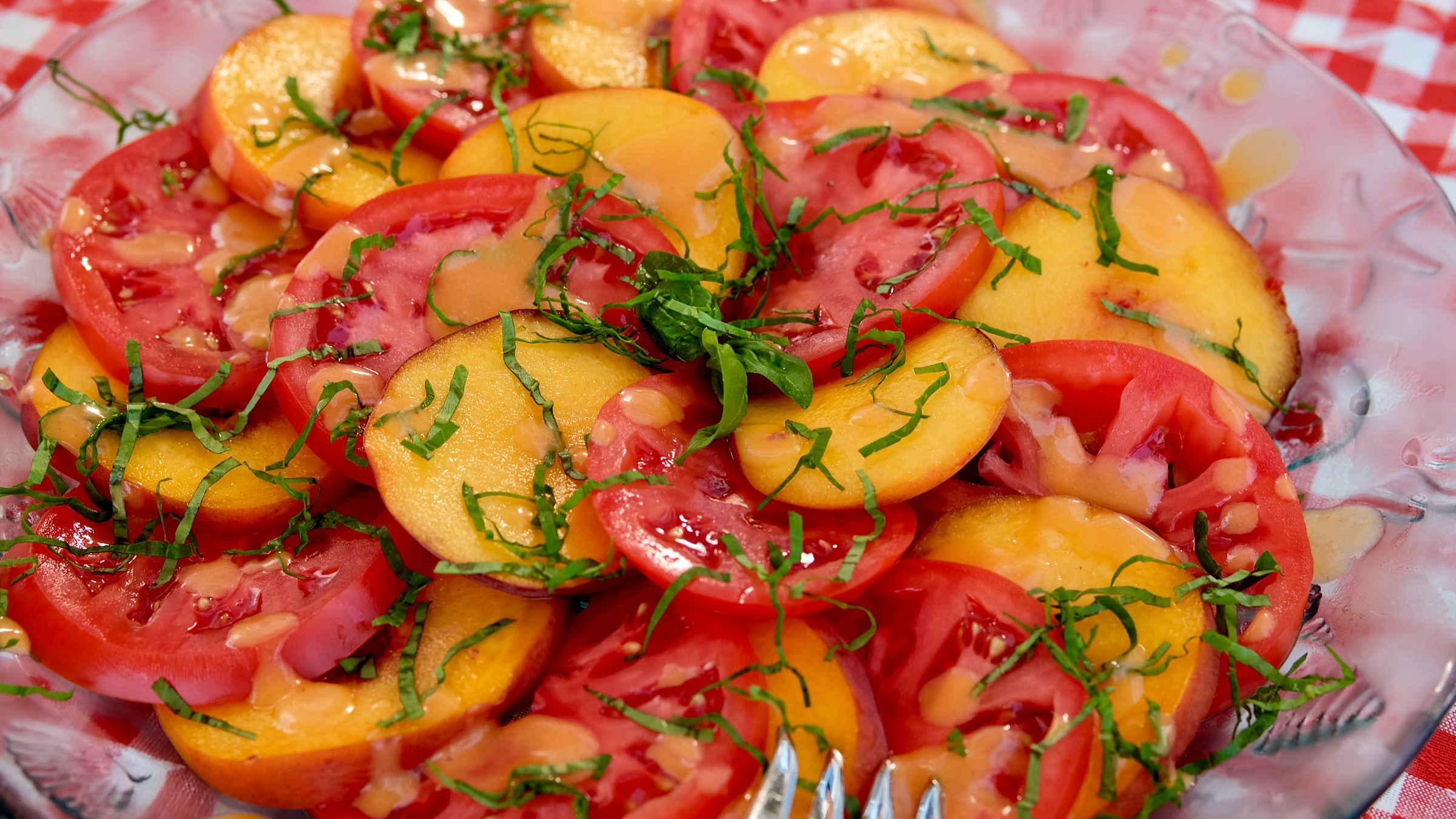 Alternating Slices of Fresh Peaches and Tomatoes layered in a circular pattern around serving platter, garnished with basil chiffonade and drizzled with fresh peach vinaigrette.
