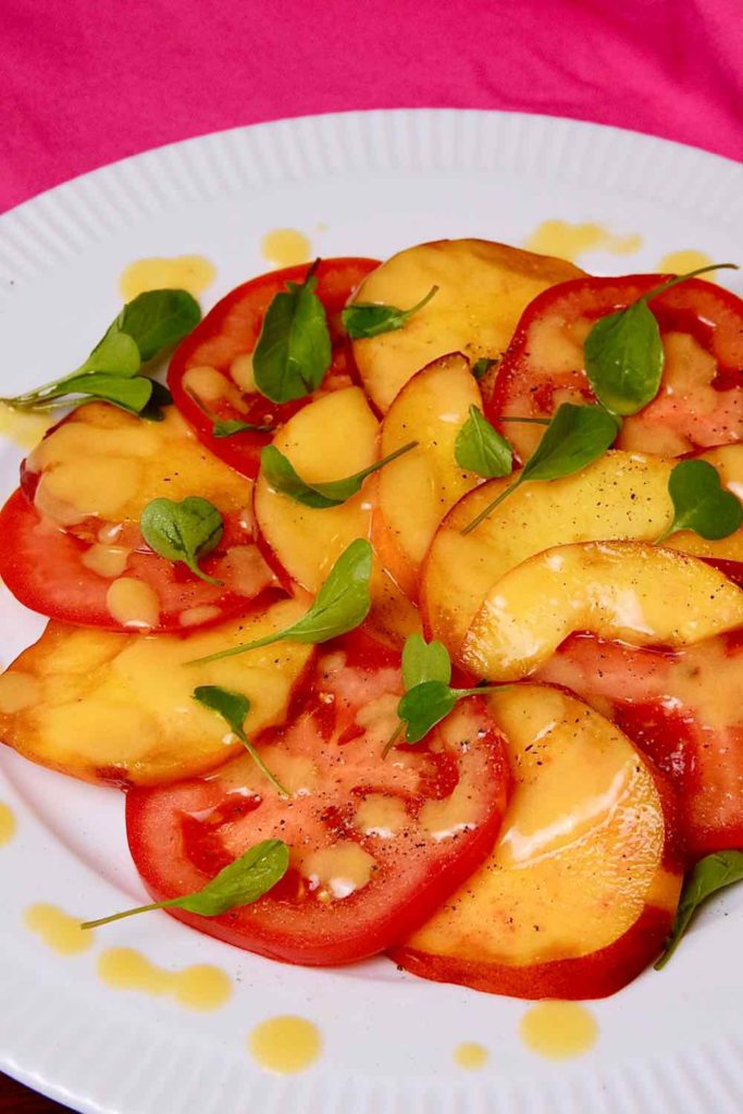 Sweet Peach and Tomato Salad on white plated drizzled with Fresh Peach Vinaigrette and garnished with baby arugula>