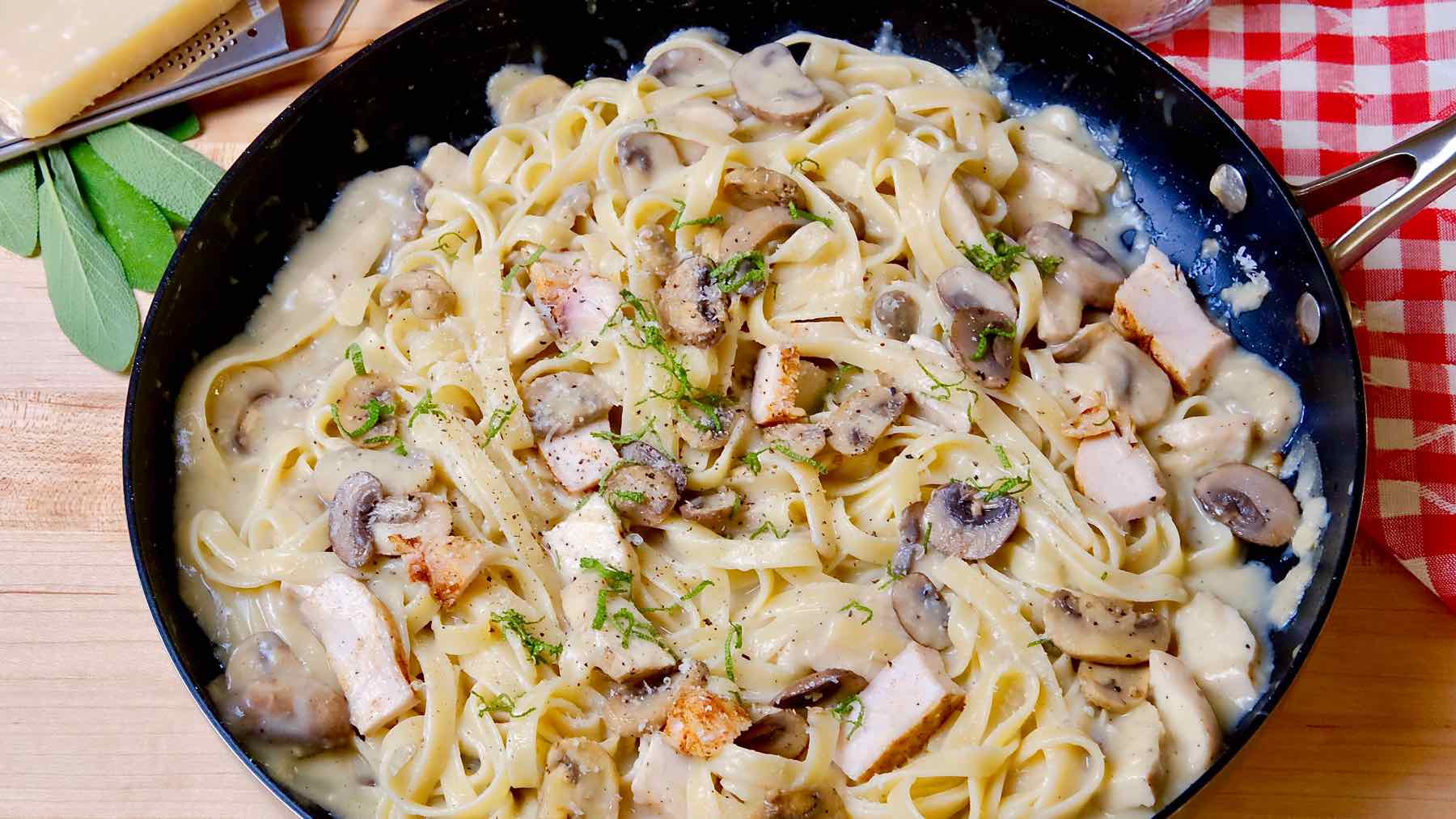 Chicken and Mushroom Fettuccine garnished with chiffonade sage in black skillet set on wood board.